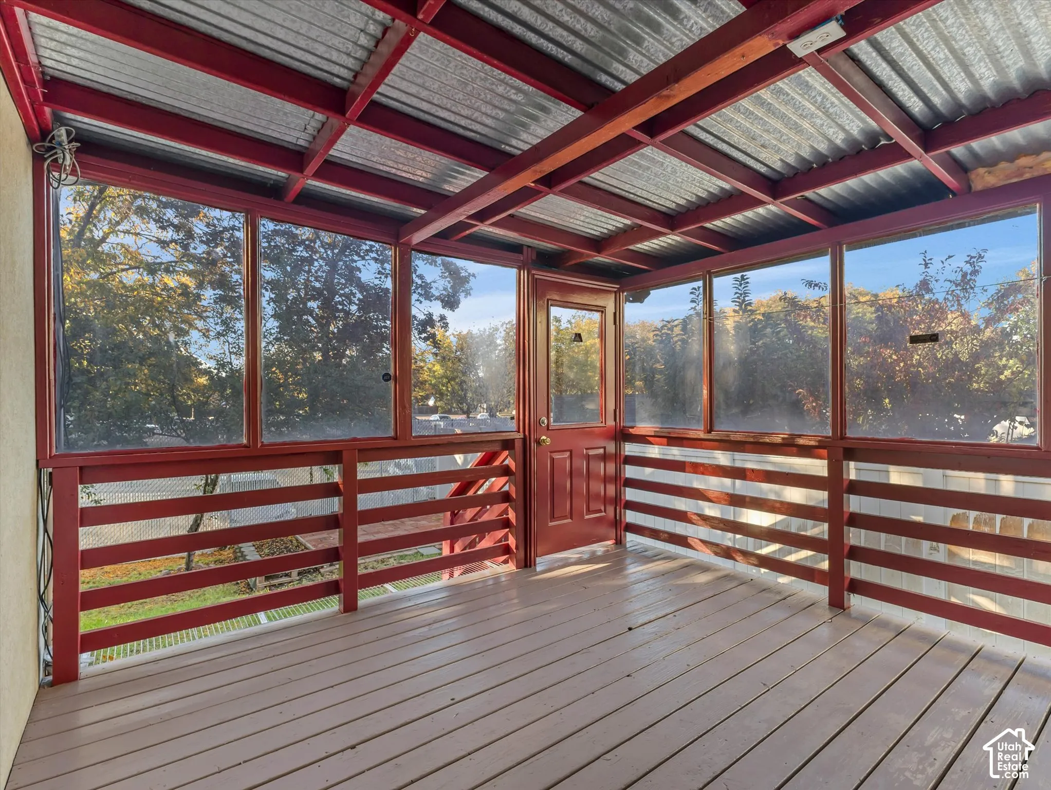 Enclosed screenedckdek featuring a corrugated metal roof, wood-finish flooring, and a red-painted door