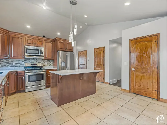 Kitchen featuring a center island with a light-toned countertop, stainless steel appliances, wood cabinetry, and tile flooring