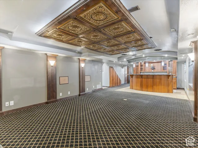 Recessed ceiling with decorative panels, built-in wet bar with wood cabinetry, patterned carpeting, and integrated wall sconces