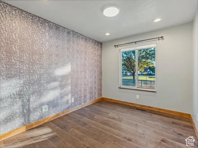 Wood-finish flooring, accent wall with textured finish, recessed lighting, and a window with natural light