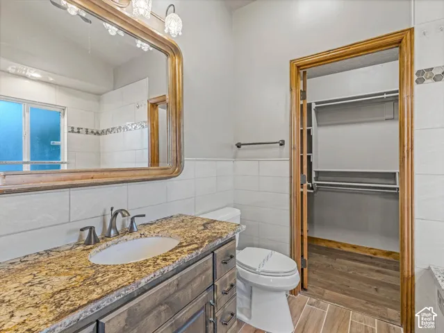 Vanity with an undermount sink and stone countertop, wood-finish cabinet, wall-mounted light fixture, and large framed mirror