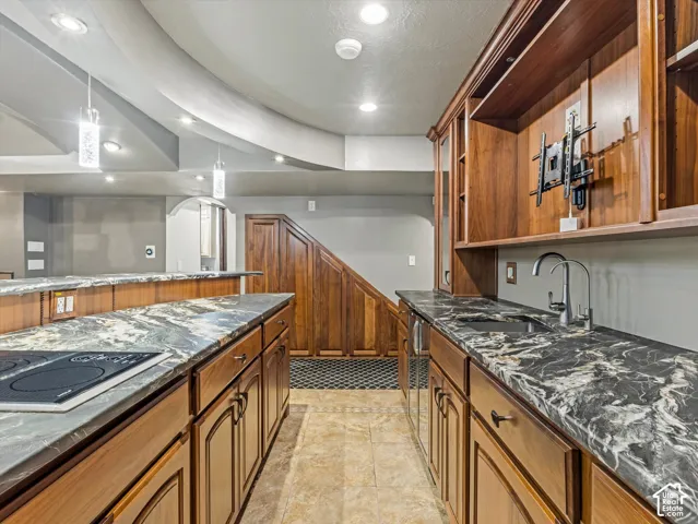 Wood-finish cabinetry, patterned countertops, undermount sink, built-in cooktop, and recessed lighting