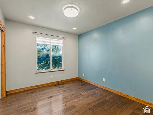 Wood-finish flooring, recessed lighting, central ceiling light fixture, window with blinds, and contrasting accent wall