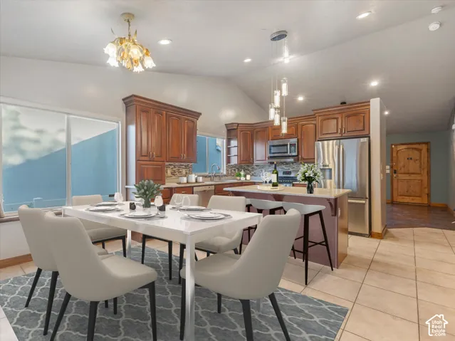 Vaulted ceiling with an ornate chandelier, a kitchen featuring wood cabinetry and stainless steel appliances, a breakfast bar, and tile flooring.Digitally Staged.