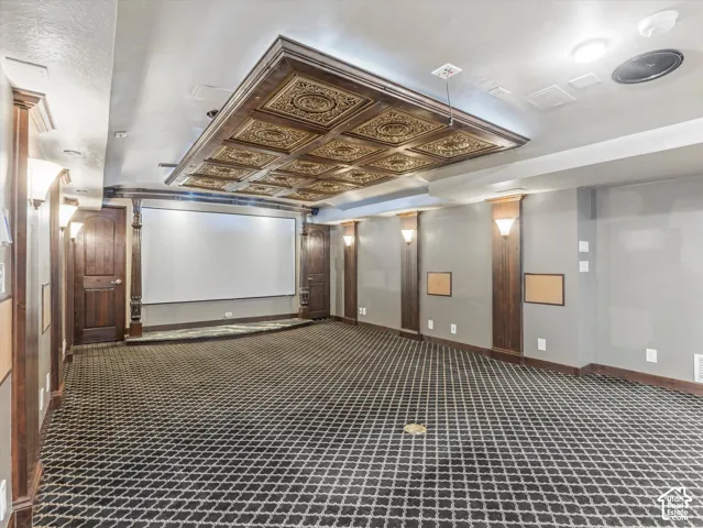 Media room featuring a large projection screen, decorative ceiling paneling, recessed lighting, and patterned carpeting