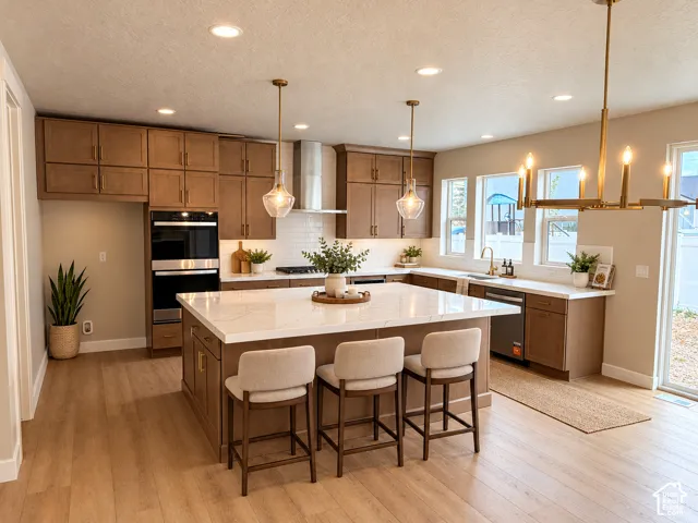 Kitchen featuring a large central island with seating, extensive cabinetry, built-in double ovens, a stainless steel range hood, and wood-finish flooring