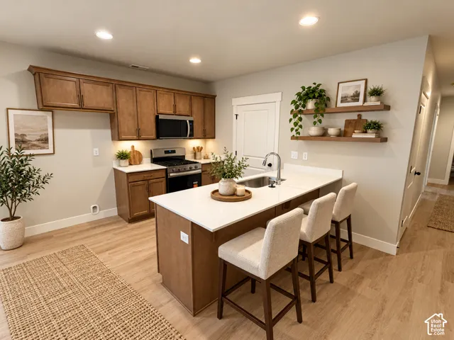 Kitchen featuring wood-finish cabinetry, stainless steel appliances, a center island with sink, white countertops, and recessed lighting