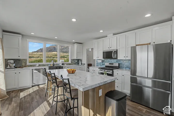 Updated kitchen featuring white shaker cabinetry, stainless steel appliances, a large center island with a stone-finish countertop, and wood-finish flooring