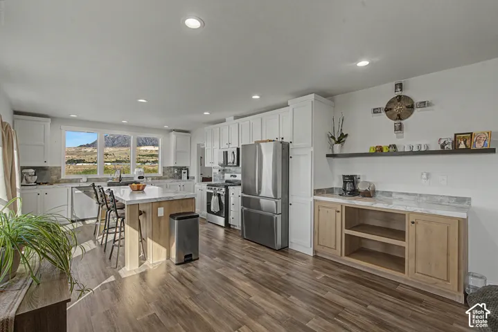 White cabinetry, stainless steel appliances, wood-finish flooring, a kitchen island with seating, and a built-in sideboard with open shelving