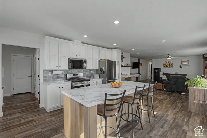White shaker cabinetry and a tile backsplash in the kitchen with a large island featuring a stone-look countertop