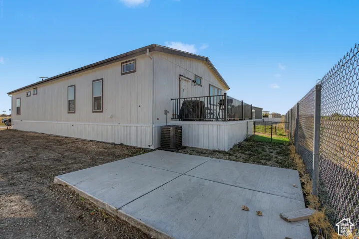 Rear exterior featuring a concrete patio, elevated deck with black railings, and a chain-link fence