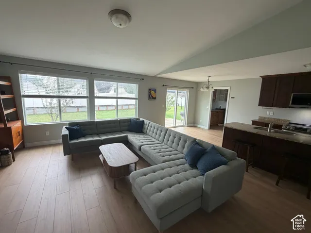 Vaulted ceiling, recessed lighting, wood-finish flooring, kitchen island with built-in sink, and sliding glass door access to the exterior