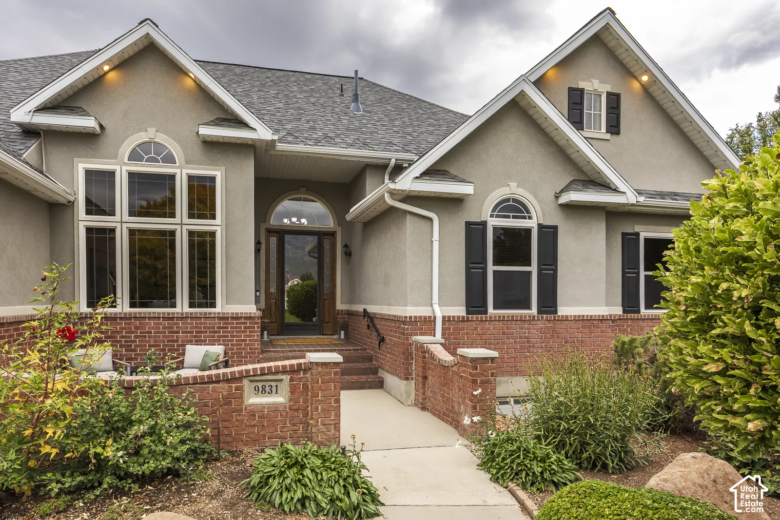 Stucco exterior with brick detailing, arched entryway, gabled rooflines, and decorative window shutters