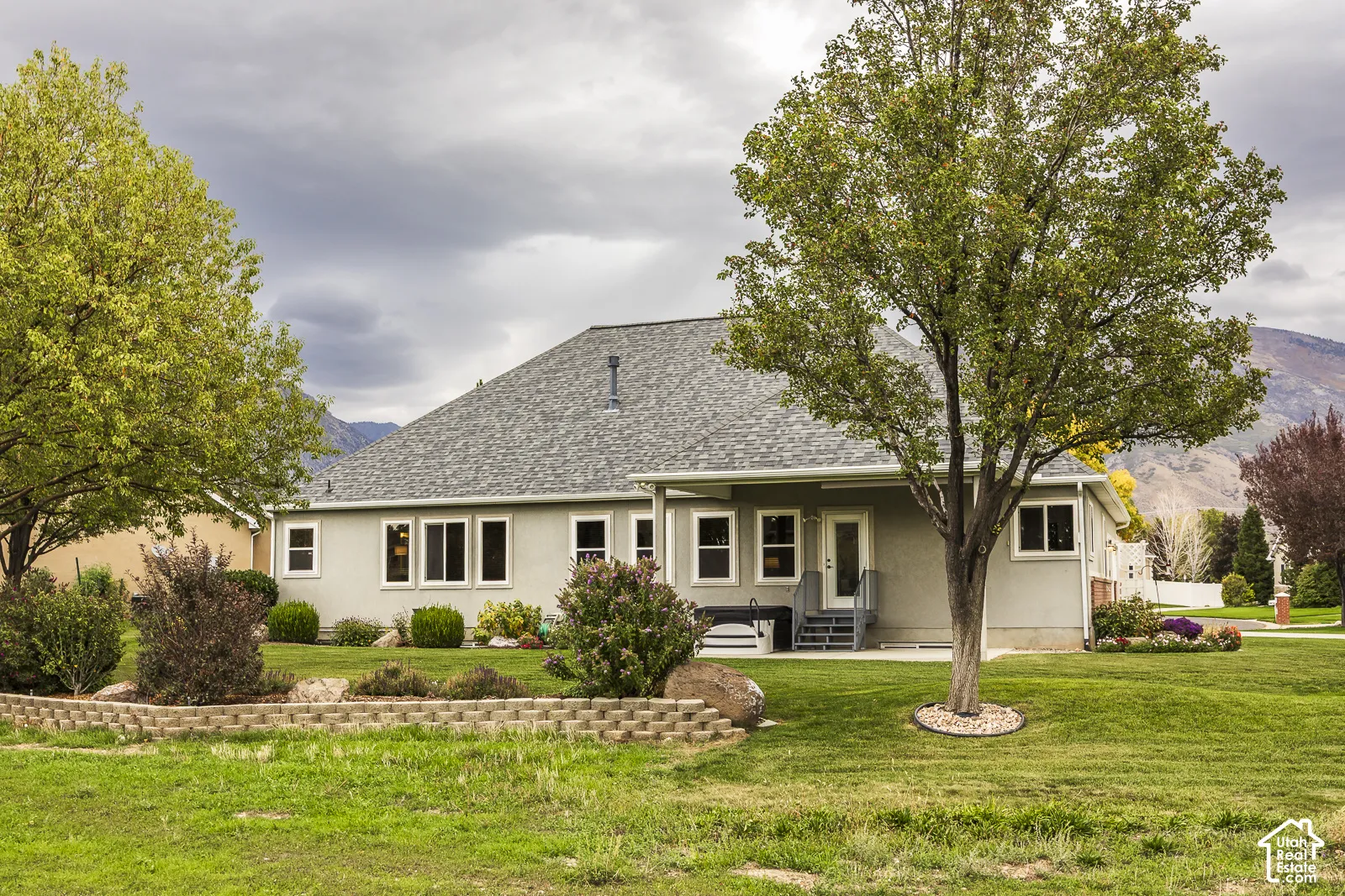 Expansive green space with mature trees, a covered patio, and a stone-lined garden bed
