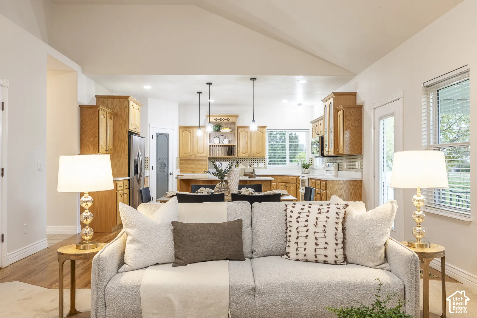 Vaulted ceiling, wood-finish flooring, light wood cabinetry, stainless steel appliances, and a pantry with a glass-paned door