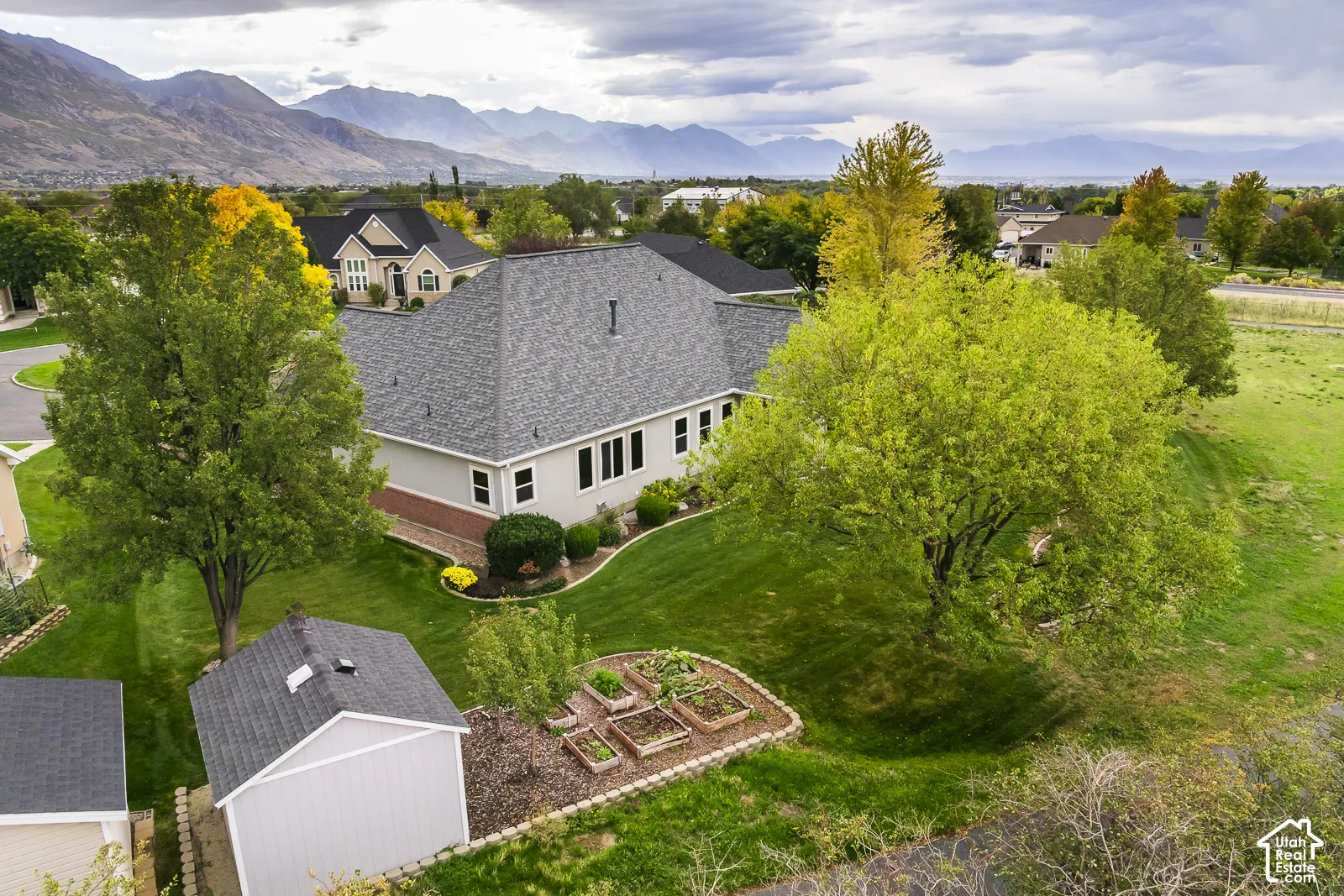 Expansive backyard with a manicured lawn, mature trees, a storage shed, and raised garden beds
