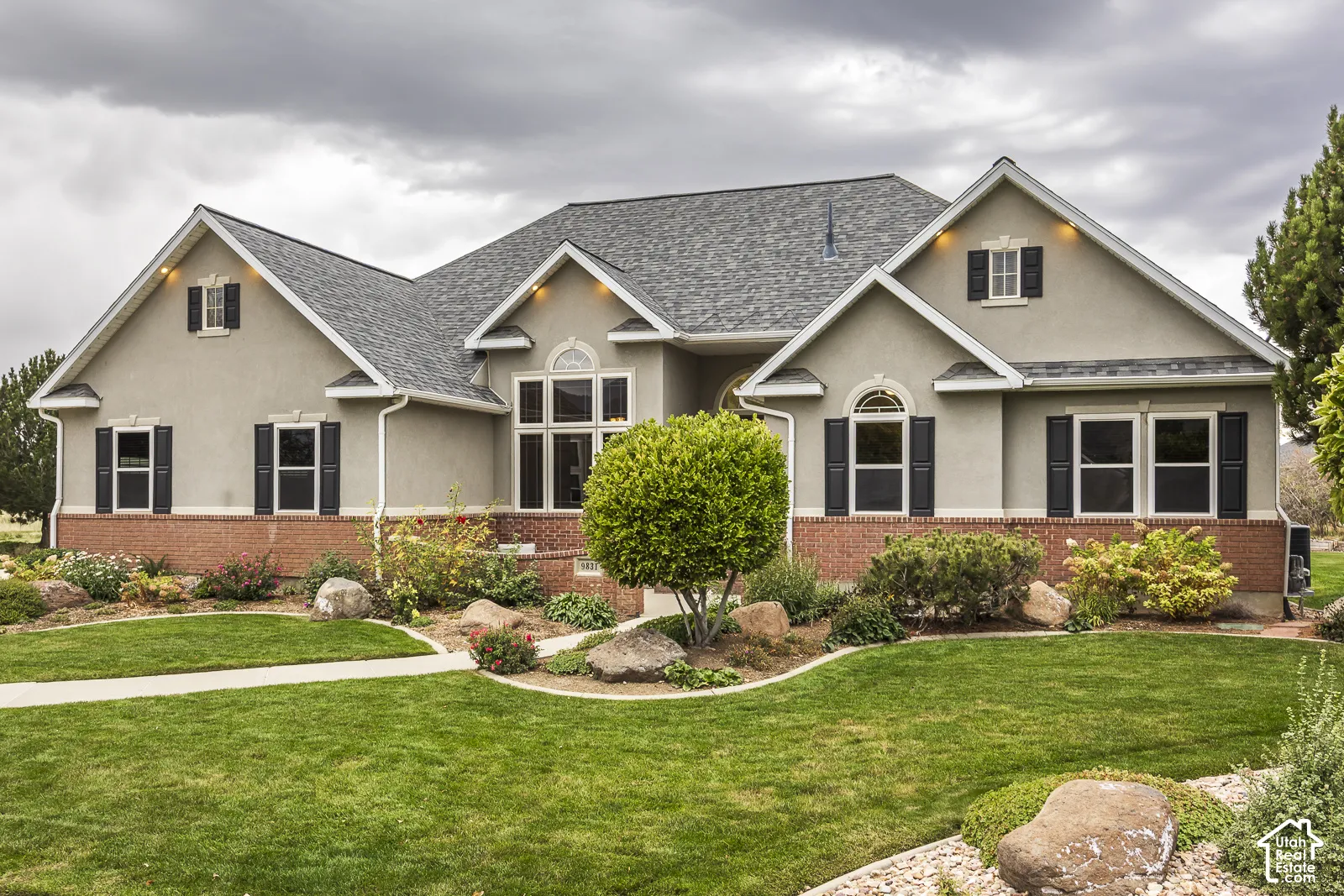 Stucco exterior with brick detailing, multi-pane windows, decorative black shutters, and an asphalt shingle roof