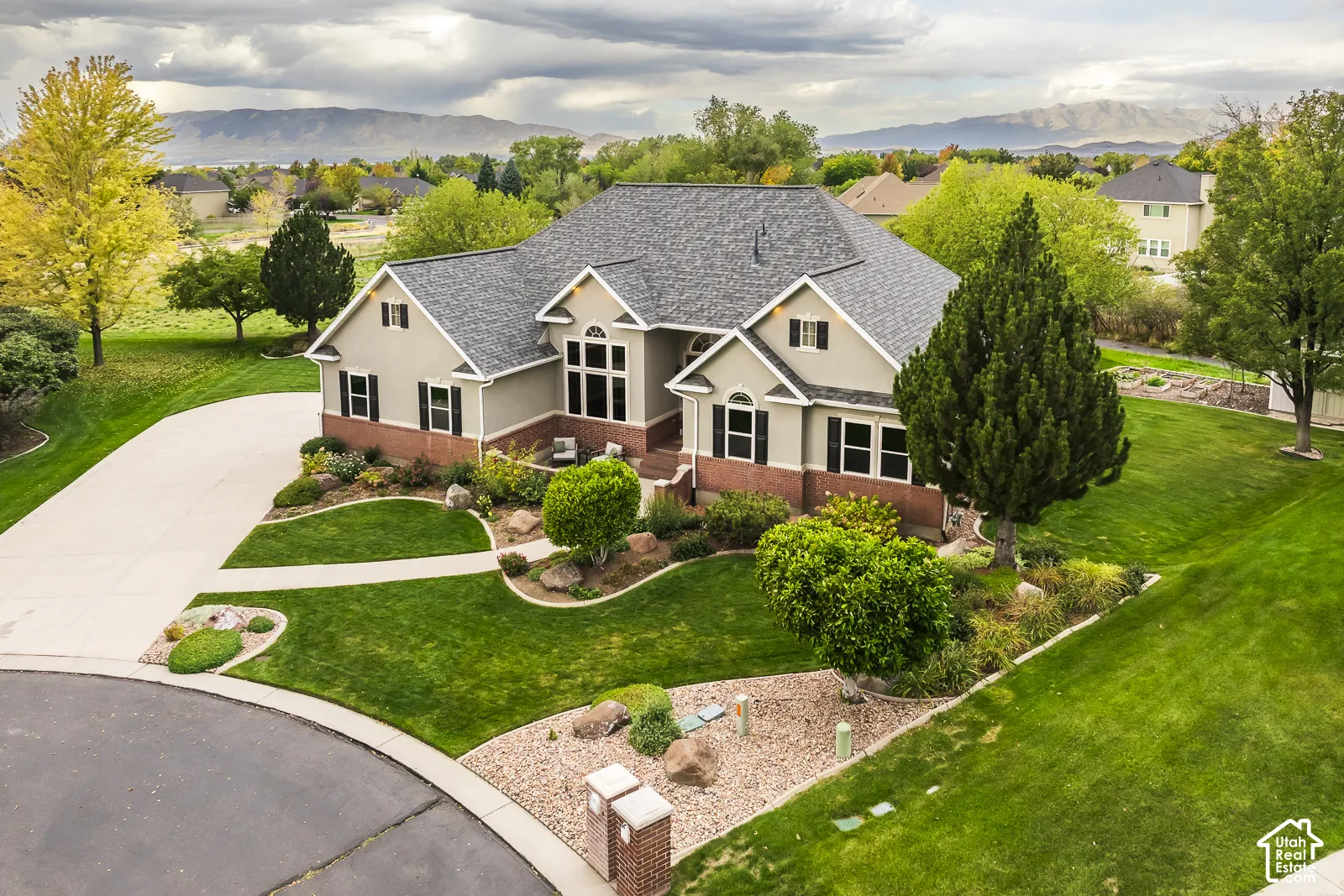 Gable roofline, light gray siding, red brick accents, dark shutters, and a concrete driveway