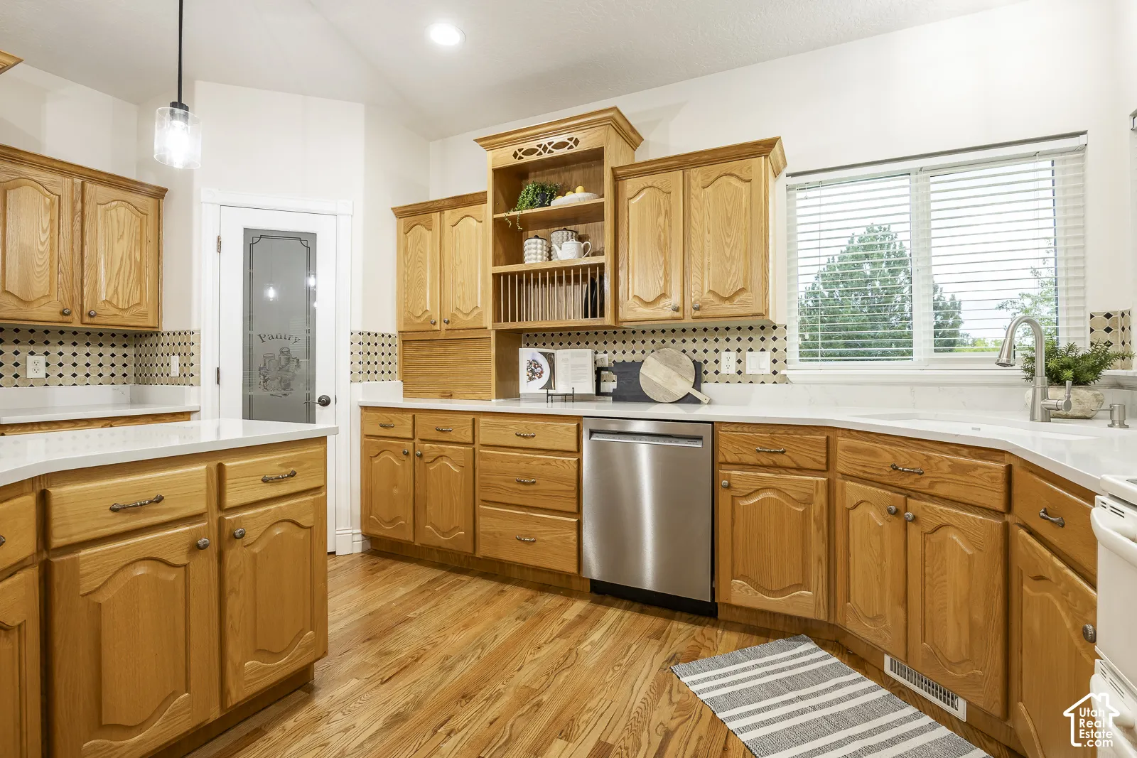 Kitchen featuring wood-finish cabinetry, white countertops, stainless steel dishwasher, and wood-finish flooring