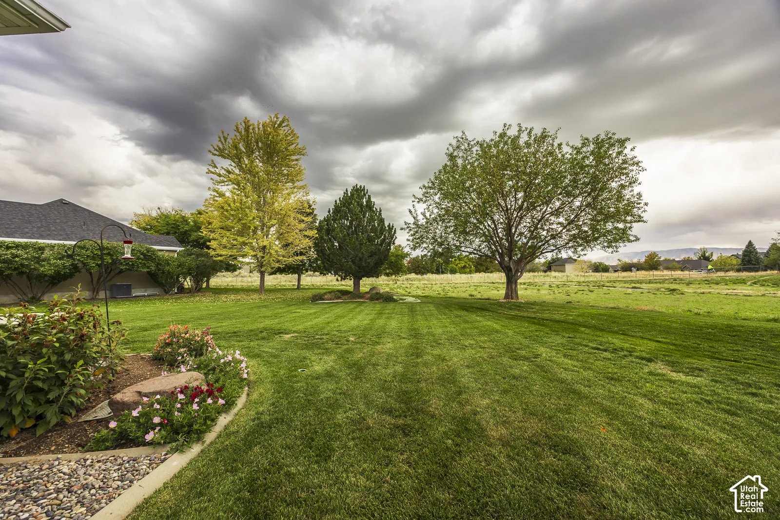 Expansive green lawn with mature trees and established landscaping featuring decorative rock and flowering plants