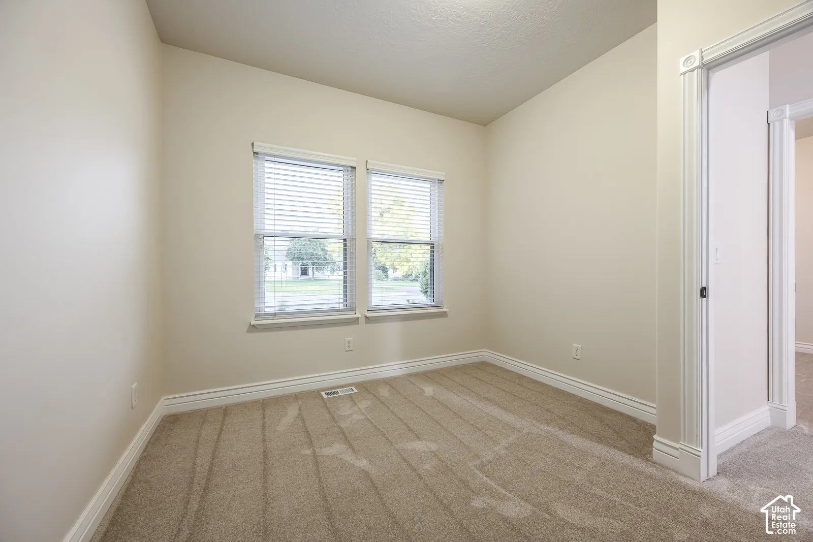 Neutral tone wall finish with two windows, light-colored carpeting, and white trim