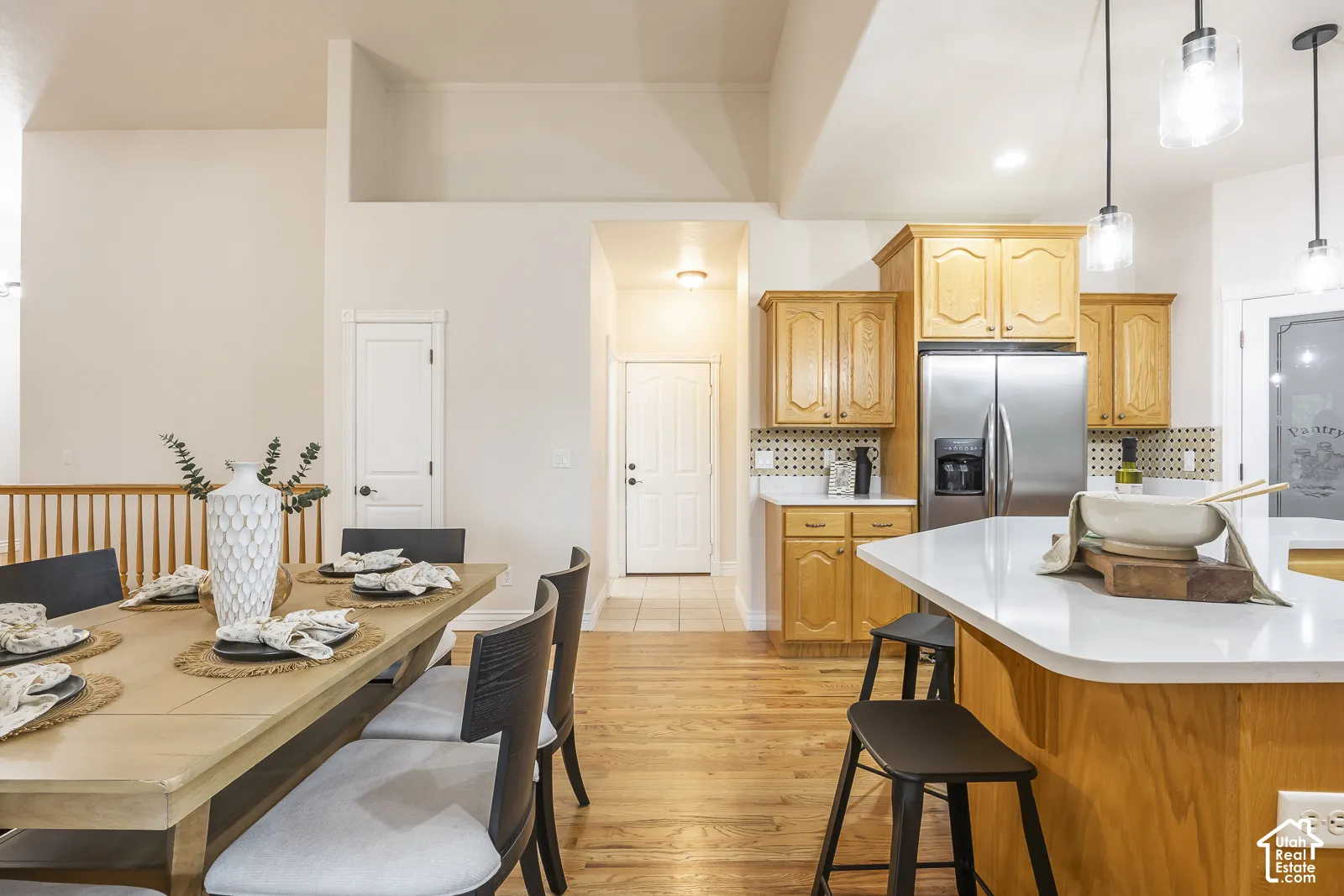 Hardwood flooring throughout, kitchen island with solid surface countertop, stainless steel refrigerator, light wood cabinetry, and recessed lighting