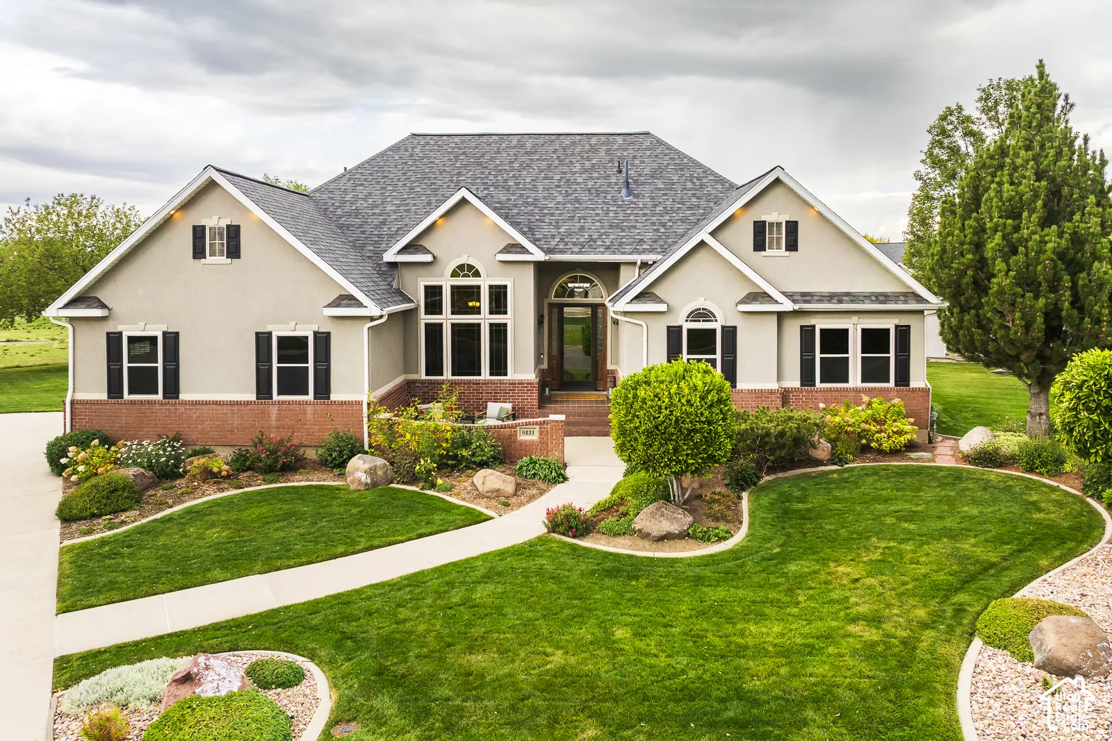 Stucco exterior with brick detailing, arched entryway, gabled roofline, and established landscaping