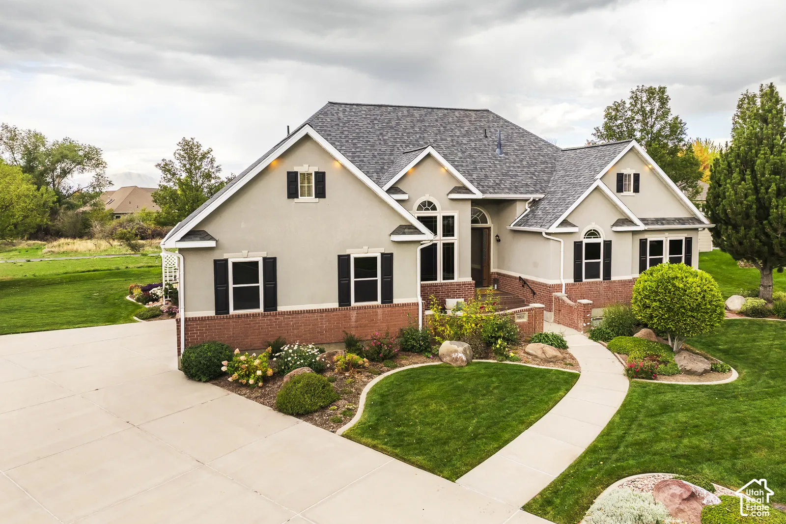 Stucco exterior with brick detailing, asphalt shingle roof, arched windows, and a curved concrete walkway