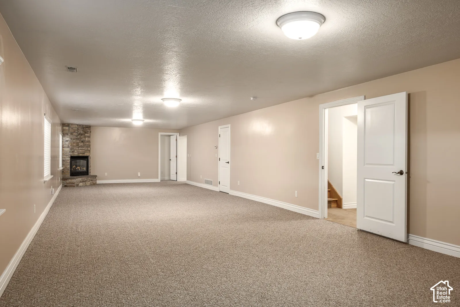 Spacious room featuring carpeting, a corner stone-clad fireplace, and recessed lighting