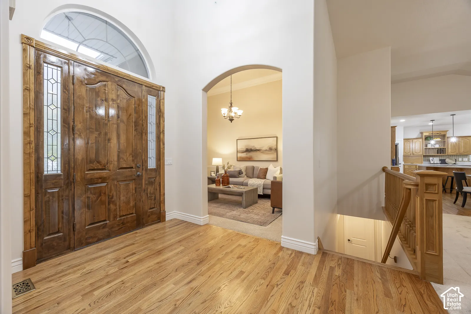Hardwood flooring, arched doorways, a wooden entry door with leaded glass sidelights, and an arched transom window