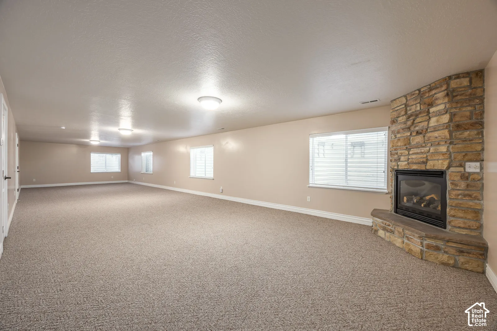 Expansive carpeted room featuring multiple windows, recessed lighting, and a corner stone-clad fireplace