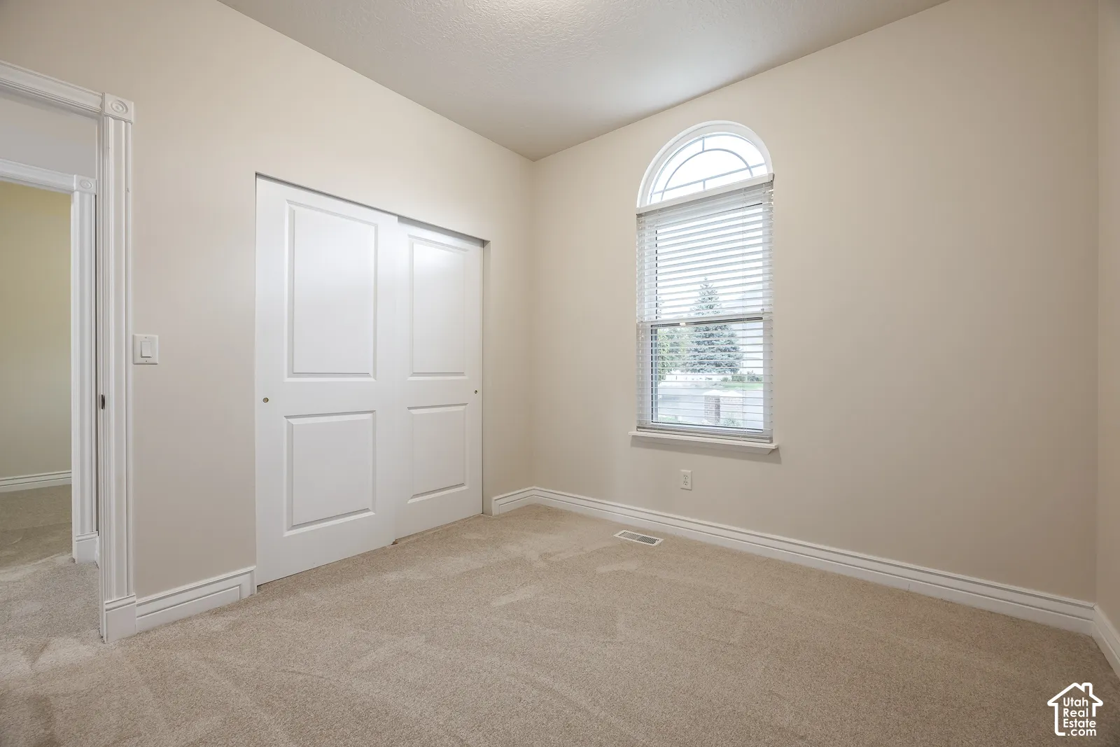 Arched window with blinds, bi-fold closet doors, neutral wall paint, and beige carpeting