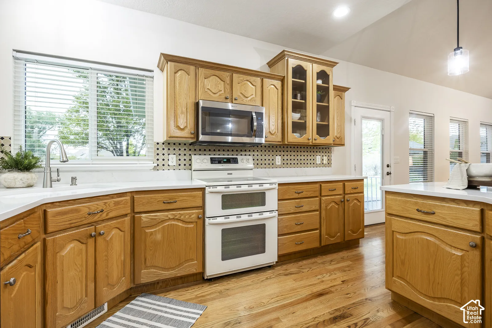 Wood-finish flooring, light wood cabinetry, white countertops, built-in stainless steel microwave, and a double oven range