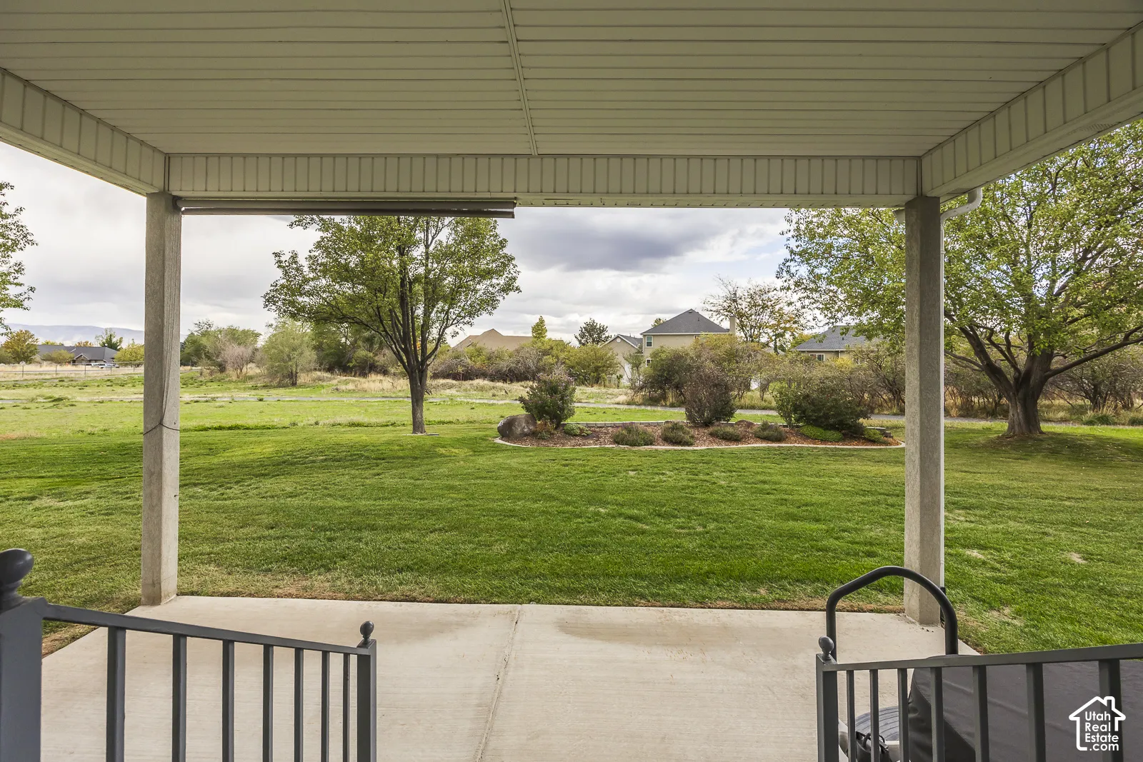 Covered patio with concrete flooring, black metal railing, and expansive green lawn