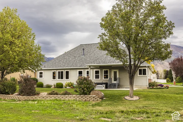 Expansive green space with mature trees, a covered patio, and a stone-lined garden bed