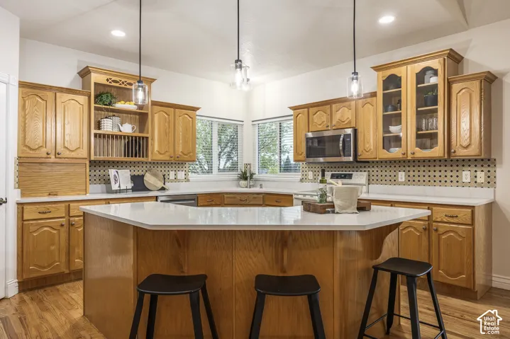 Kitchen featuring wood-finish cabinetry, a central island with countertop seating, stainless steel microwave, and pendant lighting