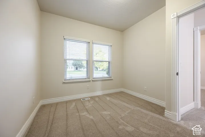Neutral tone wall finish with two windows, light-colored carpeting, and white trim