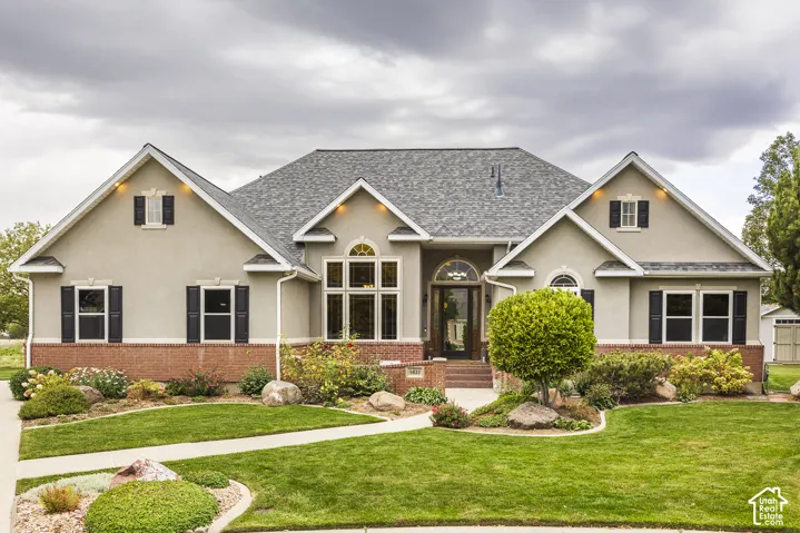 Stucco and brick exterior with a pitched shingle roof, decorative black shutters, and arched windows