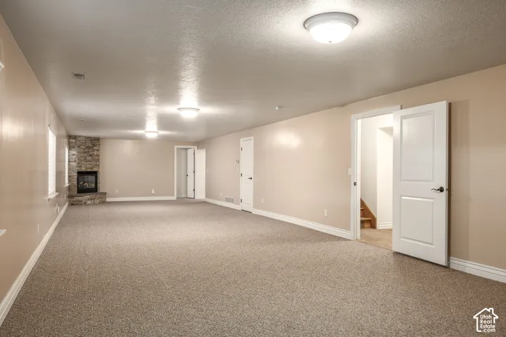 Spacious room featuring carpeting, a corner stone-clad fireplace, and recessed lighting
