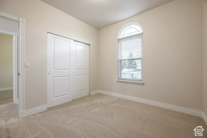 Arched window with blinds, bi-fold closet doors, neutral wall paint, and beige carpeting