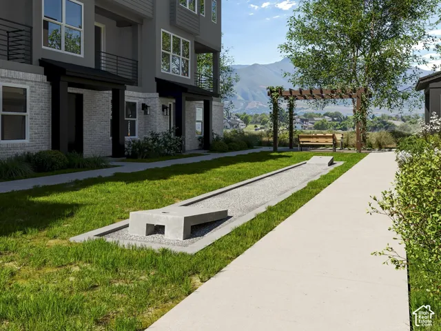 Landscaped grounds featuring a bocce ball court, concrete pathways, and a wooden pergola with seating