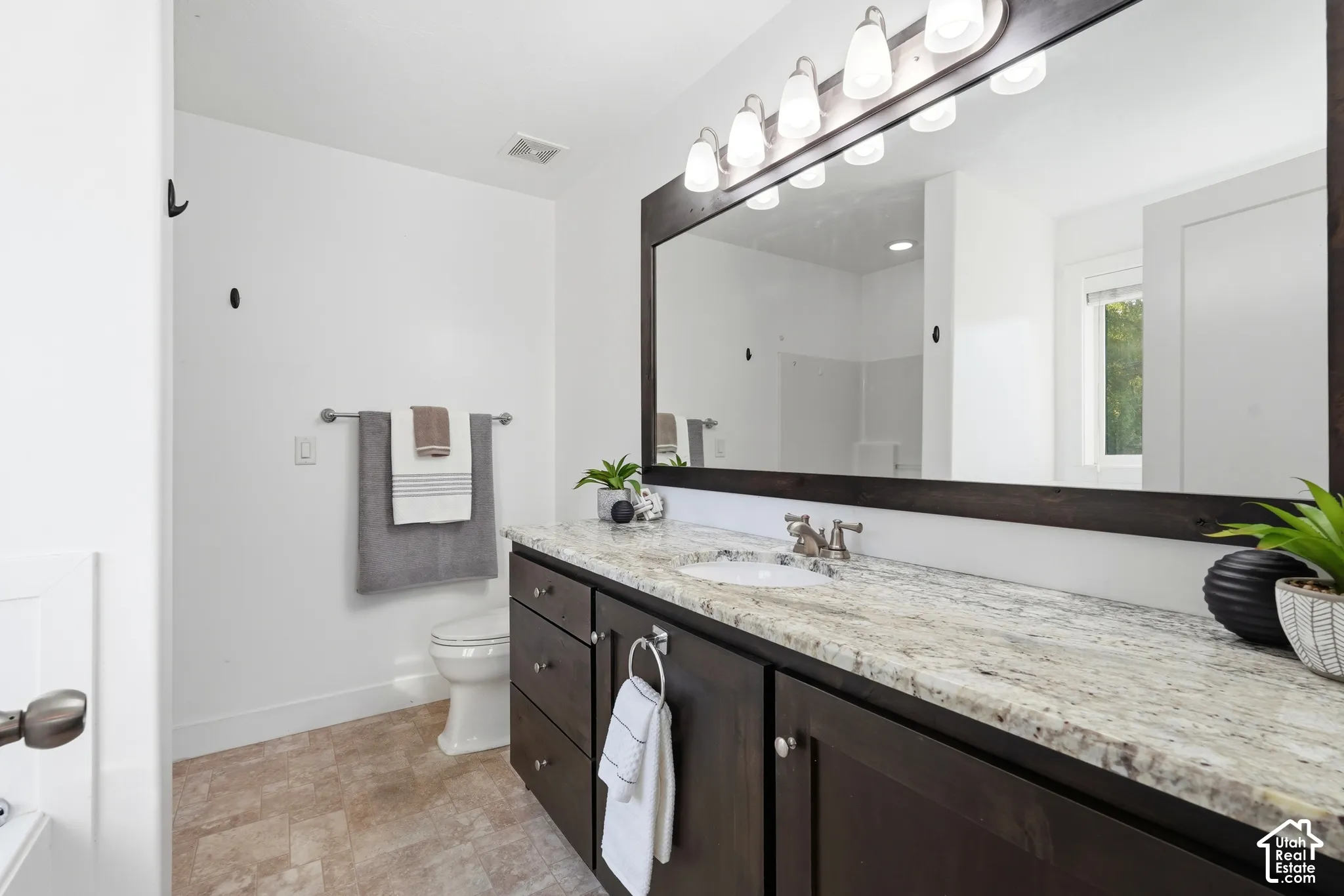 Spacious vanity featuring a light-toned countertop, a single basin sink, and dark wood-finish cabinetry