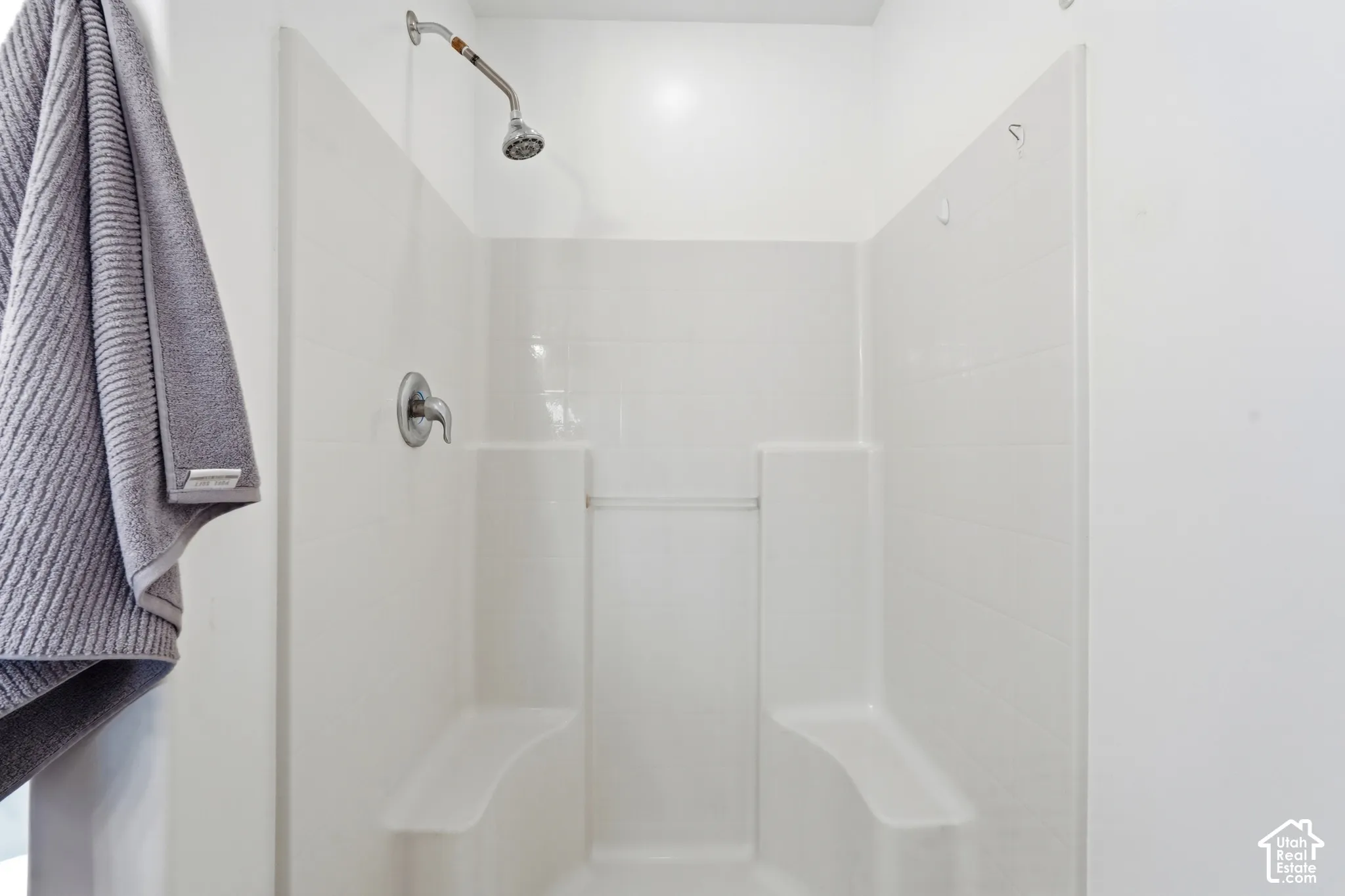 White shower stall featuring a chrome shower head and control, and two integrated benches