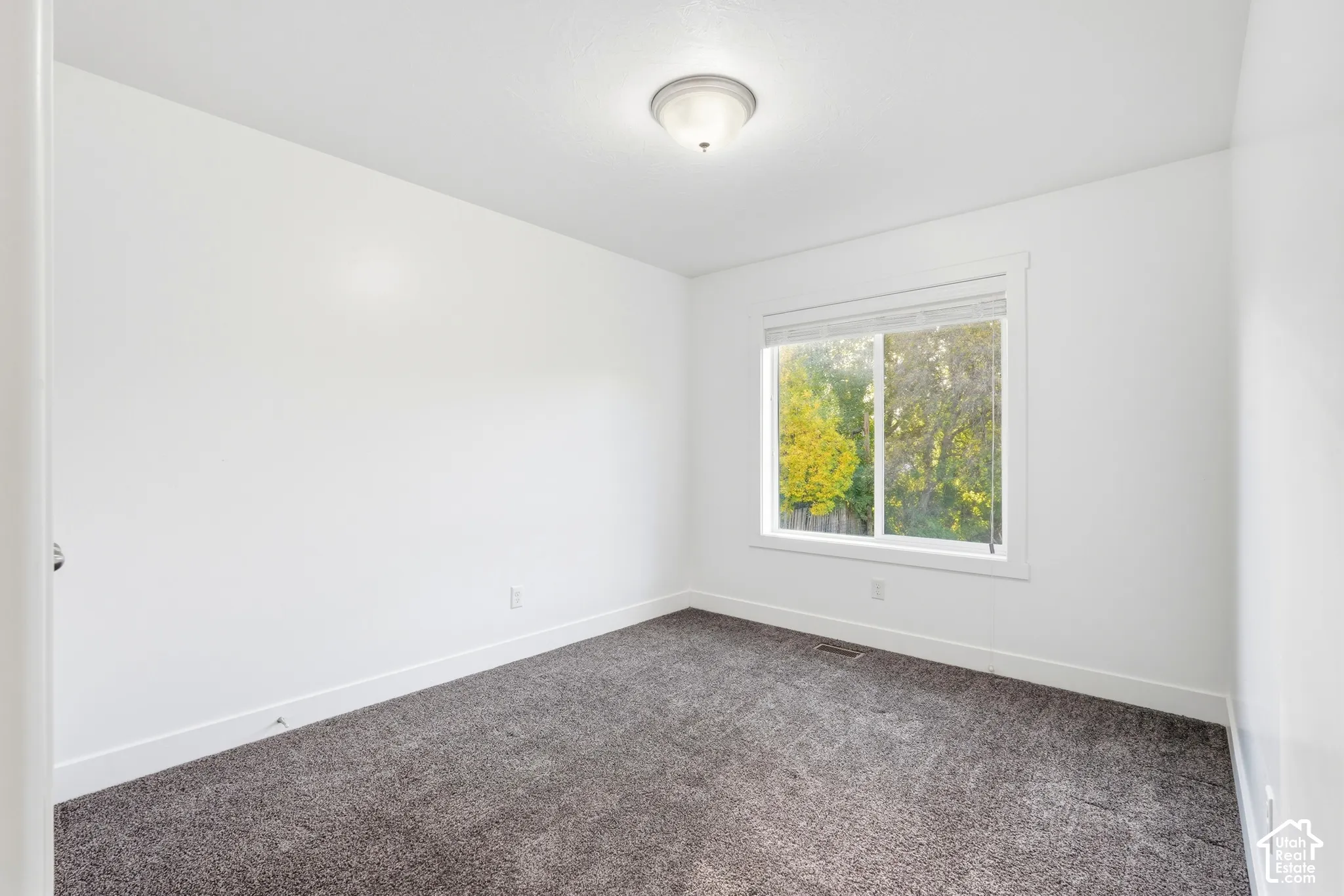 Neutral paint palette, window with exterior scenery, overhead flush mount light fixture, crisp white trim, and plush carpeting