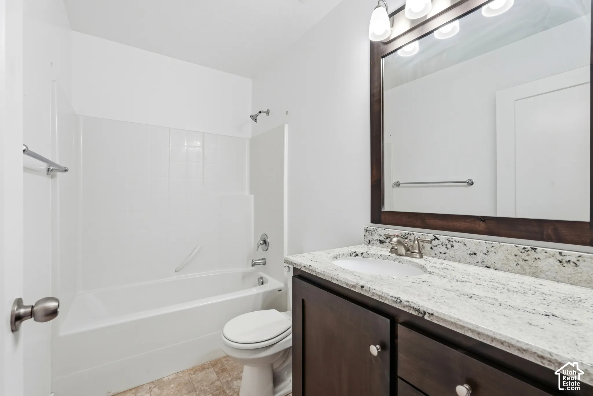 White bathtub with shower, dark wood-finish vanity with light countertop, and a framed mirror