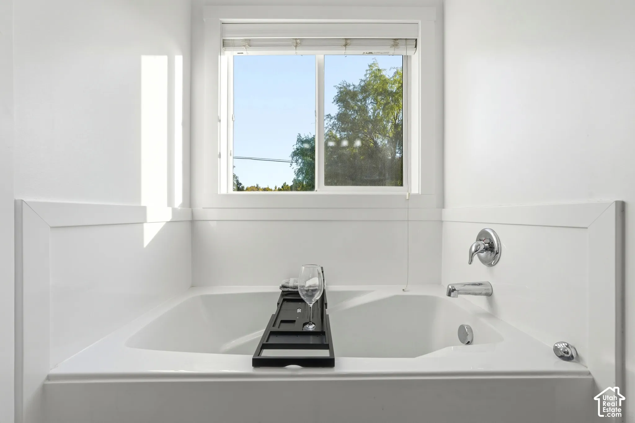 Built-in soaking tub with chrome fixtures, window with natural light, and paneling detailing