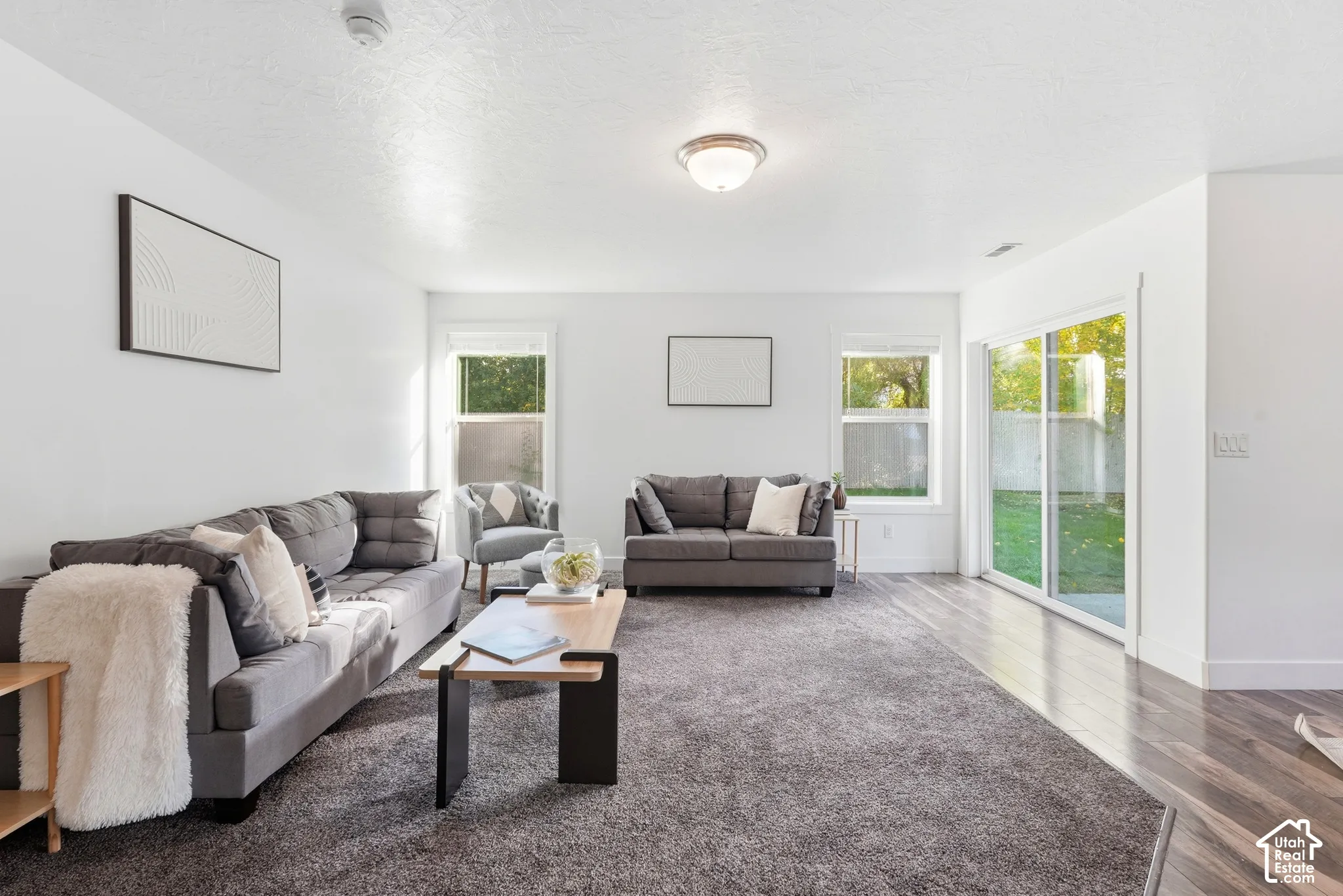 Neutral white wall paint, flush mount ceiling lighting, a sliding glass door, a window with white trim, and wood-finish flooring