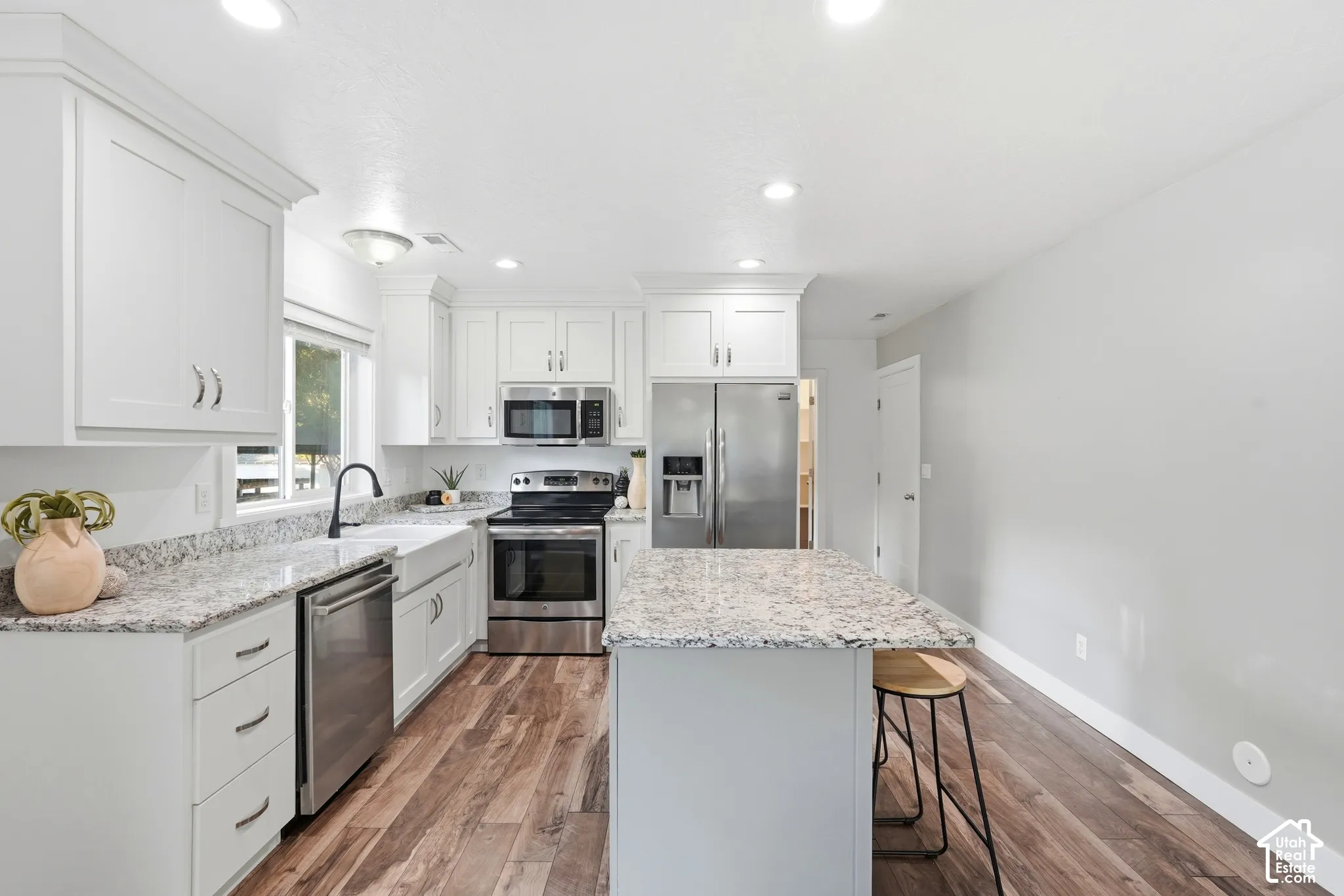 White shaker-style cabinetry, light-colored countertops, stainless steel appliances, wood-finish flooring, and a kitchen island with seating