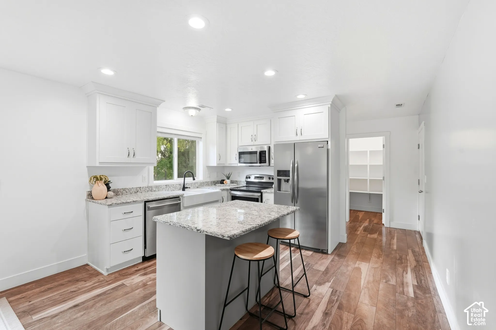 Kitchen featuring white cabinetry, granite countertops, stainless steel appliances, a center island, and wood-finish flooring