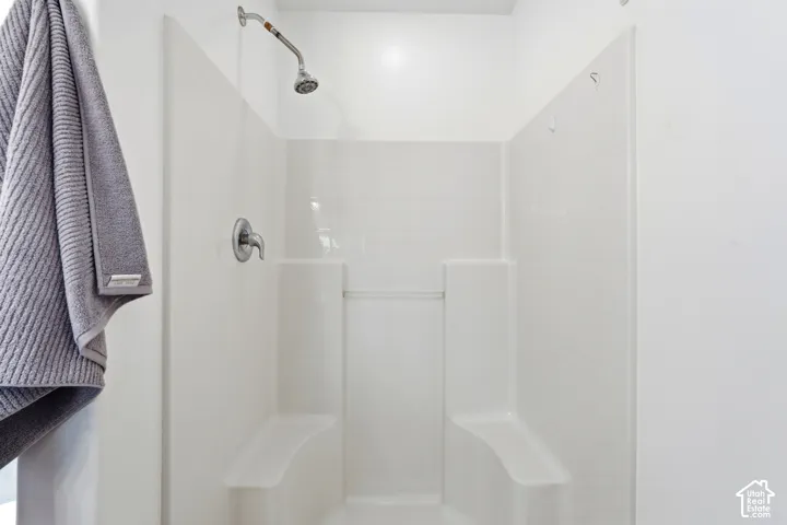 White shower stall featuring a chrome shower head and control, and two integrated benches